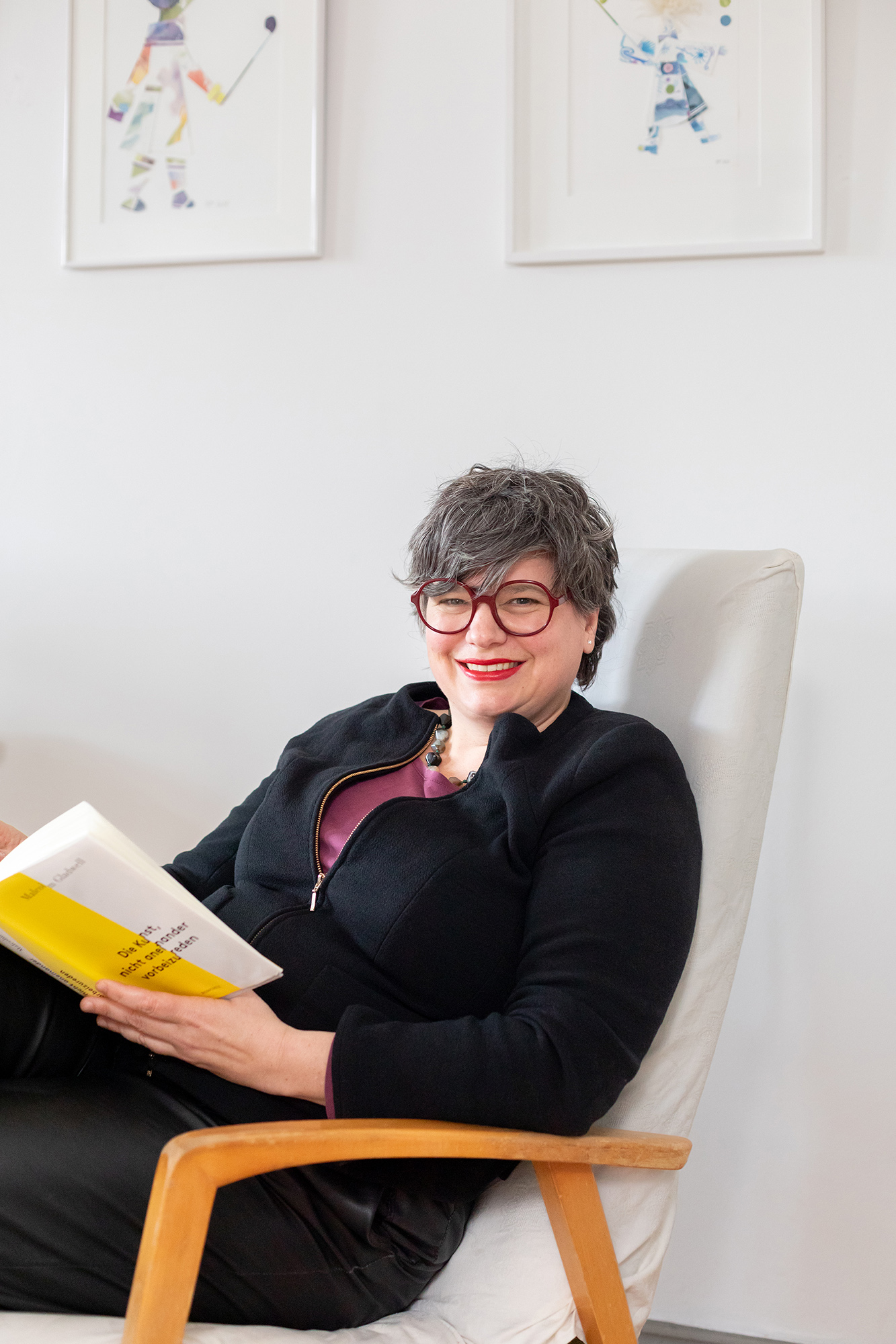 Anja Mutschler sitzt im Stuhl und lächelt in die Kamera. Sie hält ein Buch.